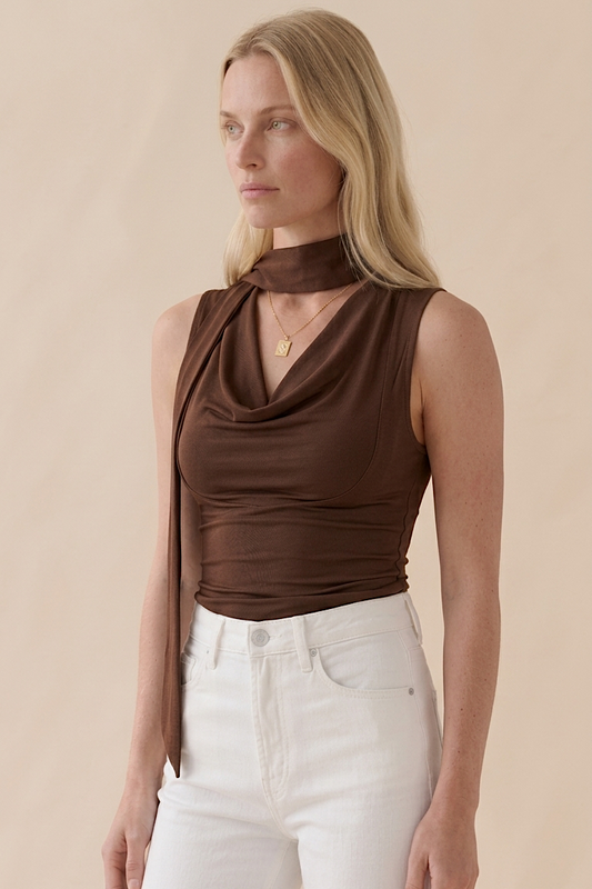 Woman wearing a brown sleeveless top and white pants against a beige background