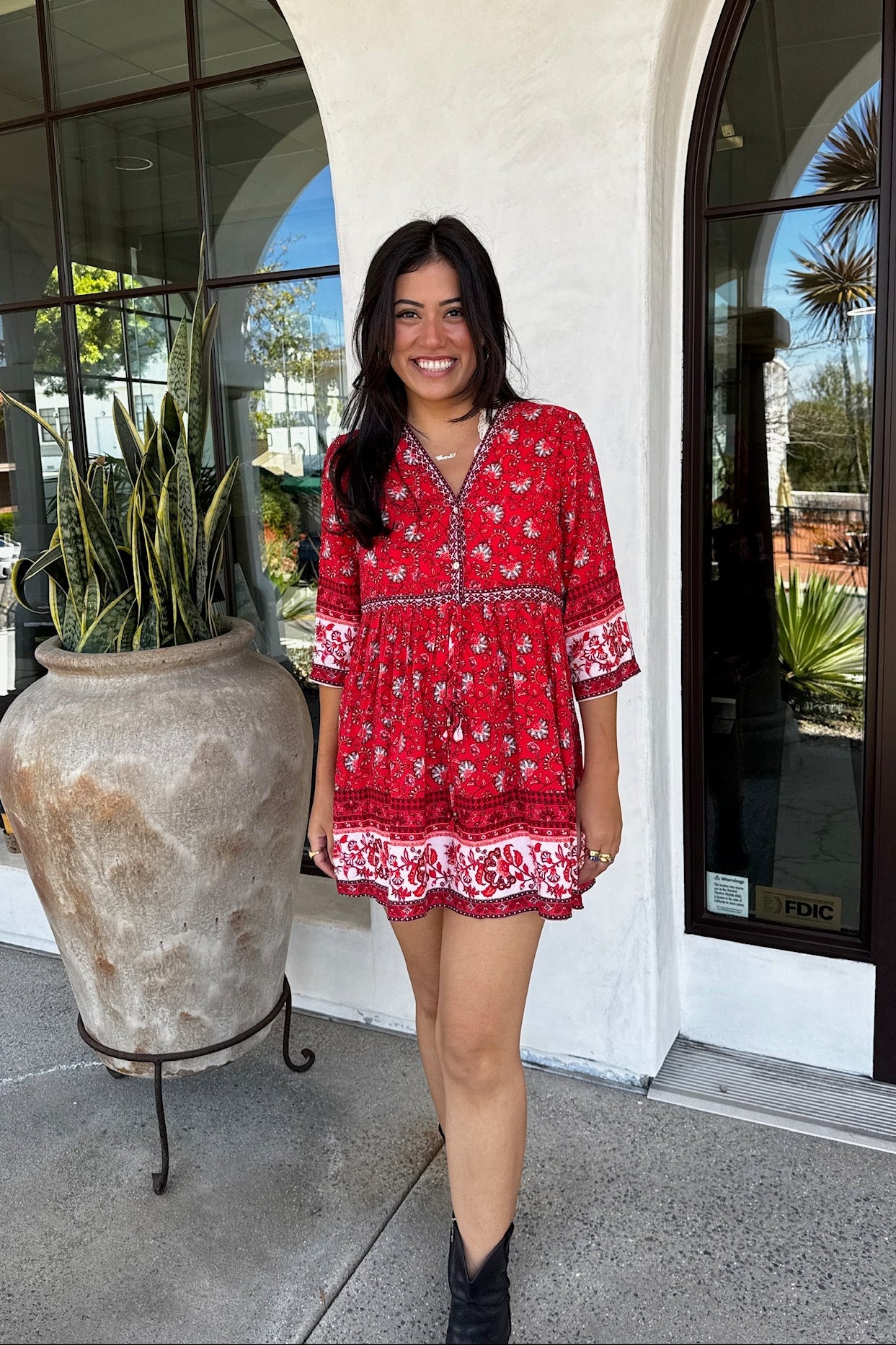 A woman standing in front of a building entrance wearing a red boho-style dress with half-length bell sleeves.