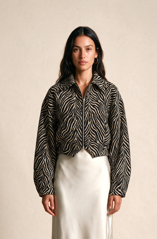 A woman stands against a plain beige studio background wearing a black-and-white abstract patterned cropped button-up shirt with long sleeves and a long white satin maxi skirt.