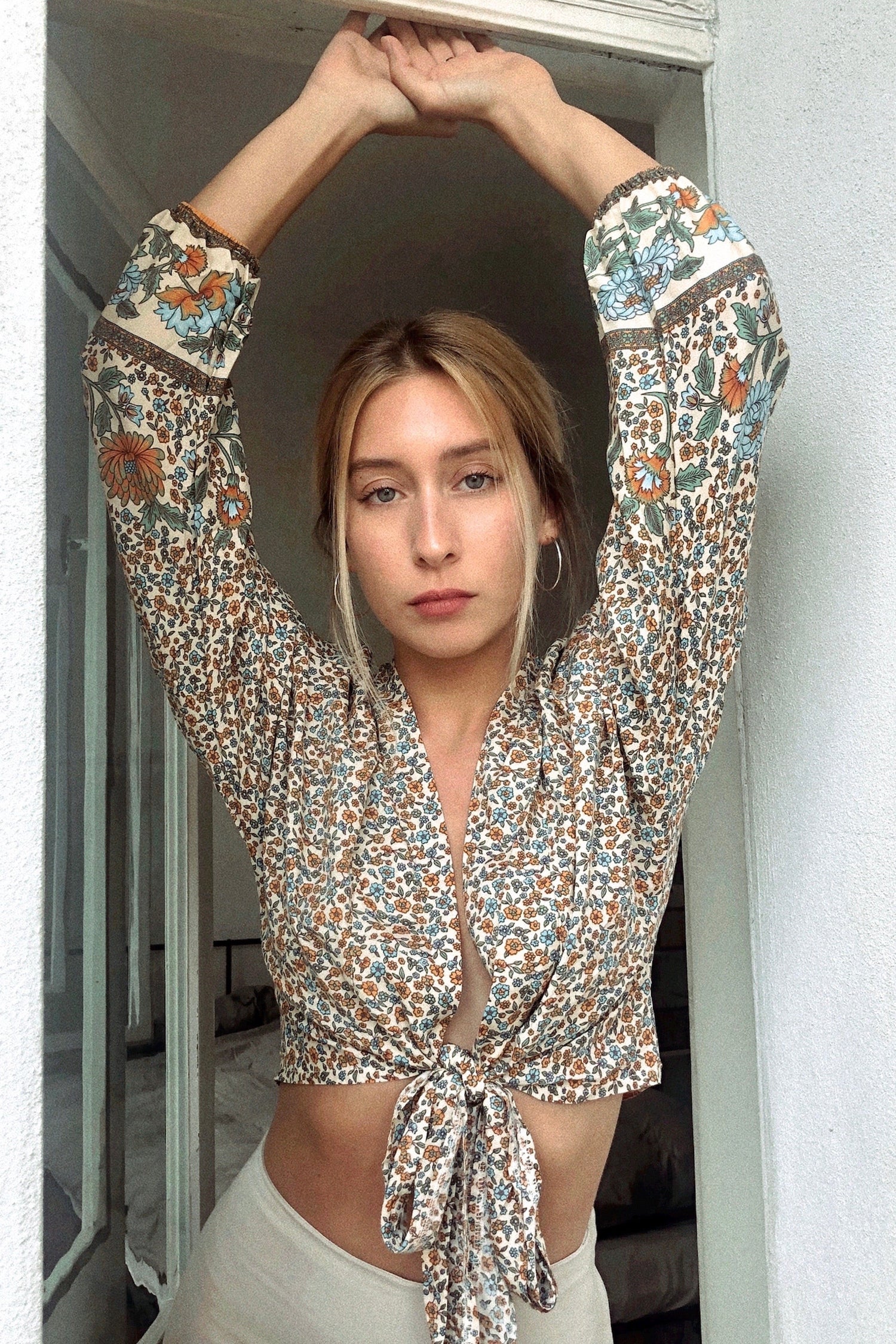 A woman wearing a boho-style top with tie floral print. The top is predominantly in shades of beige and white with a multicolor floral pattern.